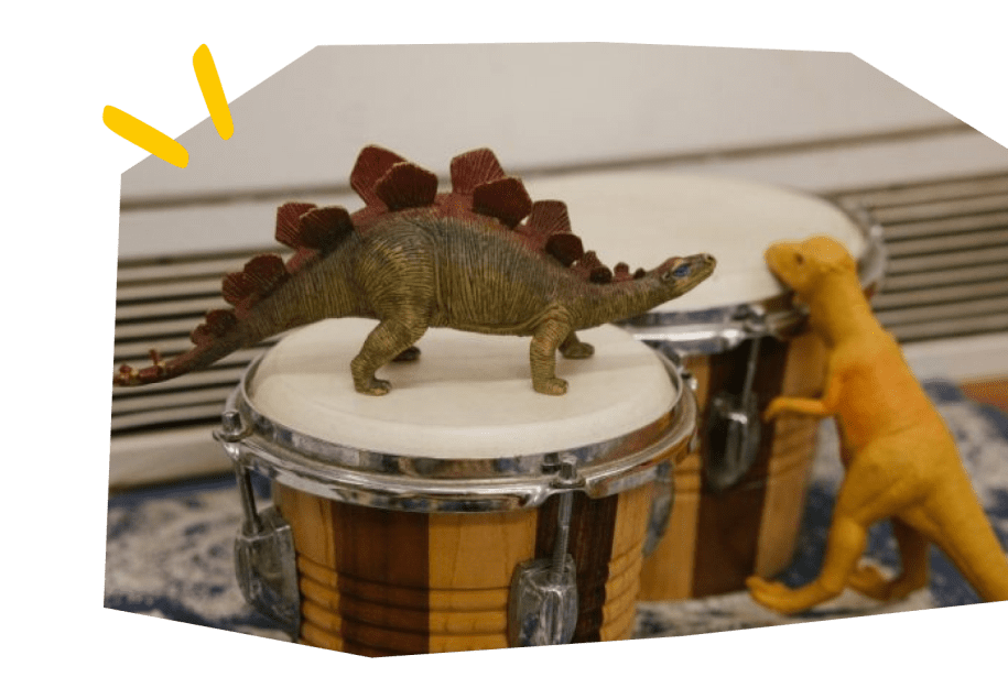A toy dinosaur on top of a pair of bongo drum.