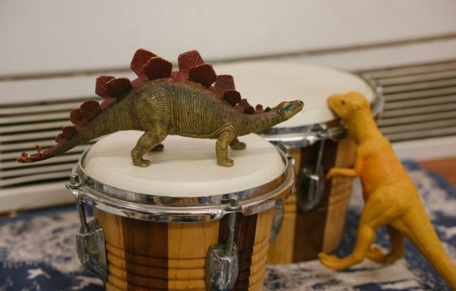 A toy dinosaur on top of a pair of bongo drum.